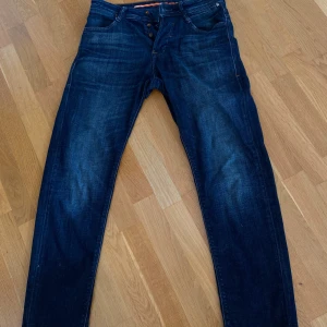Mörkblå jeans från Jack & Jones - Snygga mörkblå jeans från Jack & Jones med klassisk femficksdesign och orangea detaljer vid knappar och sömmar. Jeansen har en rak passform och är tillverkade i slitstarkt denimtyg. Perfekta för dig som gillar en stilren look.