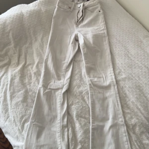 Vita bootcut jeans XS - Snygga vita jeans i bootcut-modell med hög midja. Byxorna har klassiska fem fickor, bälteshällor och stängs med dragkedja och knapp. Perfekta för dig som gillar en stilren look med lite utsvängda ben.