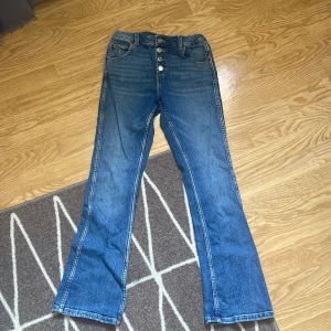 Blå bootcut jeans från Zara 164 - Snygga blå jeans från Zara i storlek 164 med bootcut passform. Klassisk femficksmodell, hög midja och flera silverfärgade knappar framtill. Jeansen är tillverkade i bomull och har en cool, tidlös look.