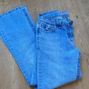 Blå bootcut jeans från Dorothy Perkins - Säljer ett par ljusblå bootcut jeans från Dorothy Perkins med snygga bronsfärgade nitar och broderade detaljer på bakfickorna. Klassisk femficksmodell med normal passform och bälteshällor. 
