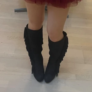 boots - Snygga svarta stövlar i mocka med högt skaft och fransdetaljer längs sidorna. Skorna har klack och rund tå, vilket ger en cool och trendig look. Perfekta för dig som vill sticka ut med din stil.