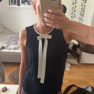 Marinblå ärmlös blus med rosett - Stilren marinblå ärmlös blus med vit prickig rosett och matchande kant vid halsen. Perfekt för dig som gillar en stilren blus. Lätt och luftig, passar till både jeans och kjol. Från Lindex märke Holly and white💗💗