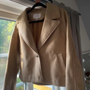 Beige kappa  från Vila - Säljer en stilren beige kappa från Vila med klassisk krage och en knapp framtill. Perfekt för dig som vill ha en clean och snygg look till vardags. Säljer då den inte kommer till användning. Kappan är bara någon månad gammal och inte använts särskilt mycket. Nypris ligger på 579kr🤗