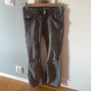 Grå bootcut jeans från Gina Tricot - Snygga grå jeans från Gina Tricot i storlek 152. Modellen har bootcut-ben och klassiska fem fickor med dubbla knappar i midjan. Jeansen är i ett mjukt bomullsmaterial och har en stilren look som passar till det mesta.