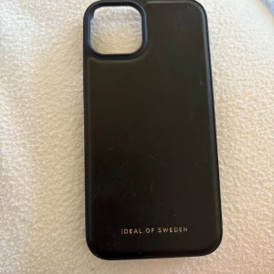 Svart mobilväska från IDEAL OF SWEDEN - Stilren svart mobilväska från IDEAL OF SWEDEN med slät yta och diskret guldfärgad logga. Väskan har en enkel, rektangulär form och är tillverkad i skinnimitation. Perfekt för dig som vill ha en clean och klassisk look till mobilen. Passar till iPhone 13