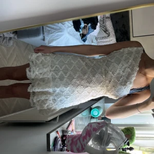 Vit spetsklänning med volang - Supersöt kort vit klänning med spets och volangdetaljer. Klänningen är ärmlös och har en öppen rygg med snygg v-ringning. Perfekt för sommarens alla tillfällen och ger en romantisk vibe.