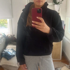 Svart hoodie med huva - En svart hoodie med huva och känguruficka framtill. Tröjan har en avslappnad passform och långa ärmar, perfekt för chill dagar. Mjuk och skön, passar till allt och är enkel att styla med jeans eller mjukisbyxor.