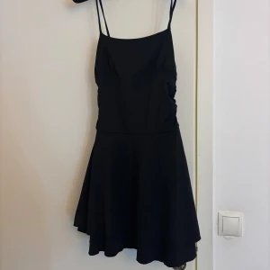 Svart kort klänning med smala axelband - En svart, kort klänning med smala axelband och lätt utställd kjol. 
