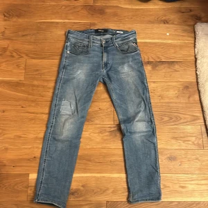 Replay Anbass - Snygga Replay Anbass jeans i klassisk blå tvätt med slitningar och ljusa detaljer. Modellen har fem fickor, raka ben och normal passform. Tidlös look med coola bakfickor och bekvämt material i bomull och jeans. Tyvärr har de ett hål i knät som är ganska synligt men det går ju alltid att sy