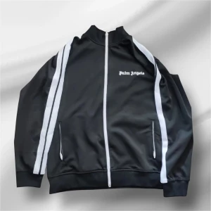 Palm Angels svart track jacket M - Svart track jacket från Palm Angels med vita ränder längs ärmarna och broderad logga på bröstet. Jackan har dragkedja framtill, ståkrage och två fickor med dragkedja. Tillverkad i 100% polyester. Den är också äkta köpt från nk och knappt använd då jag inte passar in i den. passa på och köp den innan den blir slutsåld och glöm inte att priset kan alltid diskuteras. Om du har några frågor så är de bara att skriva.🙃