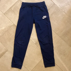Mörkblå mjukisbyxor från Nike - Hej! Säljer mörkblå mjukisbyxor från Nike med vit logga på vänster lår. Byxorna har resår i midjan, sidofickor och muddar vid vid bensluten. Tillverkade i mjukt bomullsmaterial för extra komfort. Bomull inuti för en ännu skönare känsla. Storlek 147-158 cm. Den medföljande hoodien finns också att köpa. Perfekta för chill och mysiga höstdagar! Tveka inte att höra av dig vid frågor!