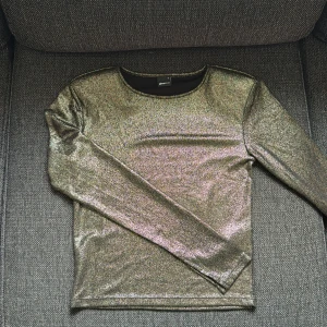 Glittrig långärmad topp Gina Tricot storlek s - Glittrig långärmad topp från Gina Tricot i storlek S. Toppen har en skimrande guldig yta och en tight passform. Även slits vid slutet av armarna och axelvadderad.