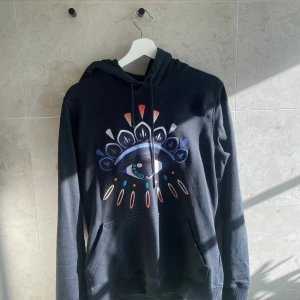 Svart Kenzo one eye hoodie  - Svart hoodie från Kenzo i storlek XS med ikoniskt broderat ögonmotiv i flera färger på bröstet. Tröjan har huva med snörning, känguruficka och långa ärmar. Perfekt statement-plagg för dig som gillar chill hoodies  och vill sticka ut.