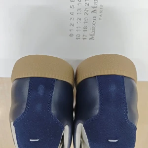 Blå sneakers Maison Margiela - Snygga sneakers från Maison Margiela i marinblå mocka och skinn med vita snören och beige gummisula. Klassisk siluett med rund tå och platt sula, perfekt för en stilren och modern look. Kommer med originalkartong.           