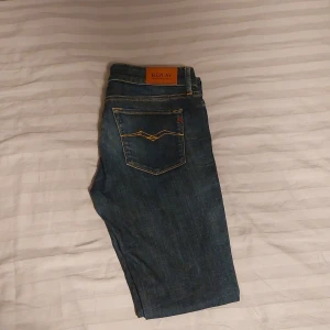 Blå Replay jeans med gul söm - Säljer ett par klassiska blå jeans från Replay med snygga guldfärgade sömmar på bakfickorna och läderpatch med logga. Jeansen har normal passform och raka ben, tillverkade i slitstarkt denim. Perfekta för dig som gillar stilrena och tidlösa jeans. Säljer dem pga att de inte längre passar mig.