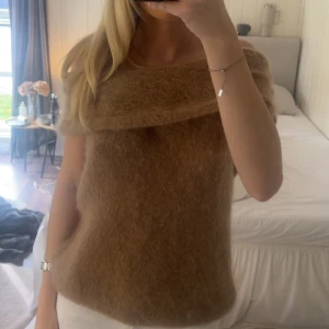 Brun stickad offshoulder topp - Säljer en fluffig brun stickad topp med offshoulder-design. Toppen har en bred krage som vilar snyggt över axlarna och är ärmlös, vilket ger en cool och trendig look. Perfekt för dig som gillar mjuka material och vill sticka ut lite extra.