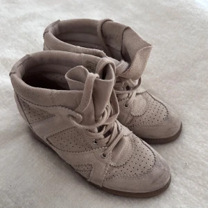 Isabel Marant liknande skor - Säljer ett par knappt använda höga beige sneakers i mocka med snygga perforerade detaljer och snörning framtill. Skorna har en rund tå och platt sula, vilket gör dem både stilrena och bekväma. Perfekt för dig som gillar en clean och soft look. Knappt använda max 3 gånger!