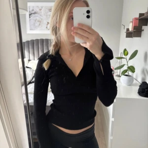 Svart ribbad långärmad  - Snygg svart ribbad tröja från Gina Tricot med v-ringad krage och långa ärmar med slits och knappdetalj vid handleden. Tröjan har en slim passform och är tillverkad i mjuk stickad bomullsmix som sitter skönt mot kroppen.