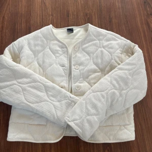 Quiltad vit jacka från Gina Tricot - Säljer en quiltad vit jacka från Gina Tricot i storlek XS. Jackan har långärmade ärmar, rund halsringning och knäpps med knappar framtill. Materialet är manchester med ett snyggt quiltat mönster som ger en cool och trendig look. använd en gång och inga fläckar