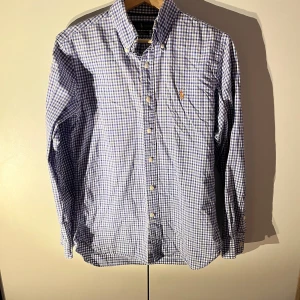 Rutig blåvit skjorta från Ralph Lauren - Snygg blåvit rutig skjorta från Ralph Lauren i slim fit-modell. Skjortan har klassisk button down-krage, långa ärmar och broderad logga på bröstet. Tillverkad i bomull och perfekt för dig som gillar en stilren och fräsch look.