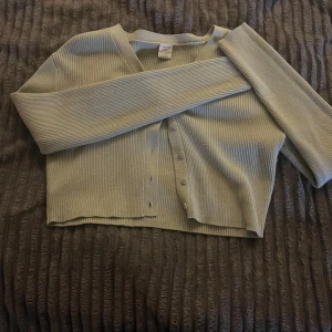 Ljusgrön ribbad kofta från Lindex - Säljer en ljusgrön ribbad kofta från Lindex med v-ringning och knappar framtill. Koftan är croppad och har långa ärmar, perfekt för lager-på-lager och chill vardagsstil.