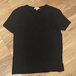 Svart basic t-shirt i bomull - En klassisk svart t-shirt från H&M i storlek M. T-shirten har rund halsringning och korta ärmar, perfekt för en clean och enkel stil. Tillverkad i mjuk bomull som är skön att bära hela dagen.