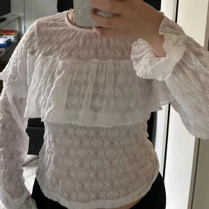 Vit blus med volang och struktur - Blusen har en bred volang över bröstet och vid ärmen, aldrig använd