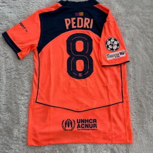 Barça Pedri #8 orange matchtröja Nike - Säljer en officiell FC Barcelona fotbollströja med Pedri #8 på ryggen. Tröjan är orange med mörkblå detaljer, klubbmärke och sponsorloggor. Korta ärmar, lätt och ventilerande material, perfekt för match eller träning.