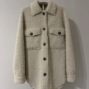 Beige teddyjacka med knappar - Säljer en oversized beige teddyjacka. Det är en två i ett jacka vilket gör att man kan bära den på två olika sätt, både med teddytyget utåt men även vända den ut och in så får man en jacka med ett slätare tyg. Varan har inga tecken på användning.