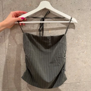 Randig grå korsettopp Tiger Mist - Supersnygg grå korsettopp från Tiger Mist med tunna axelband och knyt i nacken. Toppen har ett stilrent randigt mönster och en croppad passform. 