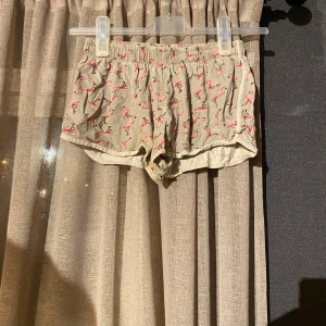 Beiga shorts med flamingomönster Primark - Säljer ett par beiga shorts från Primark med elastisk midja och ett gulligt rosa flamingomönster. De är lätta och sköna, perfekta för varma dagar eller som chill-plagg hemma. Materialet är mjukt och andas, vilket gör dem riktigt bekväma.