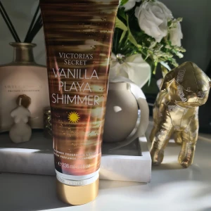 Vanilla Playa Shimmer från Victoria's Secret - Shimmer lotion med doft av vanilj, tropisk orkidé och cherimoya. Tuben är brun och guld med glittrande detaljer, innehåller 236 ml. Ger huden en skimrande finish och en tropisk, söt doft. Vegansk formula och förpackning delvis av återvunnet material. Helt ny och oanvänd svarar ej på bud.
