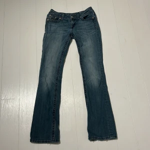 Miss Me bootcut jeans med pärldetaljer - Säljer mina miss me jeans som är low waist bootcut med snygga detaljer. Köpte för 1250kr på A2vintage och då hade redan knappen bak på ena fickan släppt och längst ner var lika upprivet som när jag köpte dom. De har även små svarta fläckar där bak men man ser dem knappt om man inte letar efter dem (kom privat för bild)           Innerbens längd = 83cm  ytterbens längd = 105cm       Tvärs över midjan =35cm 