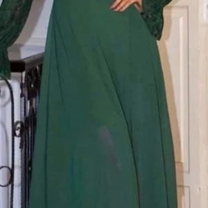 Grön långklänning med spetsärmar - Elegant grön långklänning med långa spetsärmar och vacker, svepande kjol. Perfekt för dig som vill sticka ut med en klassisk och stilren look. Klänningen har en feminin siluett och är riktigt snygg till festligare tillfällen.