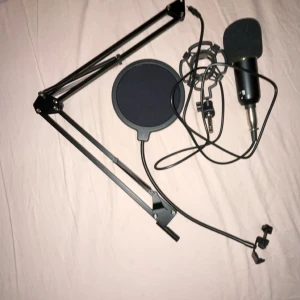 Kondensatormikrofon med stativ och popfilter - Komplett kondensatormikrofon med stativ, popfilter och stötdämpare. Mikrofonen har gulddetaljer och medföljer kabel med 3,5 mm kontakt. Allt ser ut att vara i gott skick utan synliga defekter eller slitage. Perfekt för streaming, podcast eller inspelning.