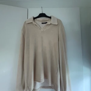 Beige pikétröja från J.Lindeberg - Säljer en stilren beige pikétröja från J.Lindeberg i mjuk frotté. Tröjan har klassisk krage, v-ringning och långa ärmar. Perfekt för dig som gillar en clean och avslappnad look.