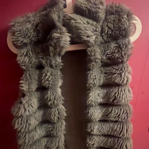 Grå fluffig pälsimitation väst - Supermjuk och fluffig väst i grå pälsimitation. Den har en cool, ruggad struktur med breda ränder och ger en riktigt mysig vibe. Perfekt för kalla dagar när du vill sticka ut och hålla dig varm.