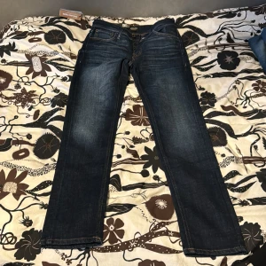 Mörkblå tapered jeans Jack & Jones storlek 29/32 - Snygga mörkblå jeans från Jack & Jones i modellen Tapered/Mike. Jeansen har klassisk femficksdesign, orangea sömmar och en tapered passform som smalnar av nedtill. Tillverkade i slitstarkt denimtyg som ger en cool look. Storlek 29/32 helt nya med lappen kvar!