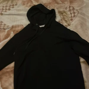 Svart Givenchy hoodie med logoband - Svart hoodie från Givenchy med vita logoband längs ärmarna. Klassisk huva med snörning och långärmad modell. Snygg streetstyle-vibe och perfekt för dig som gillar exklusiva märken och stilrena detaljer.