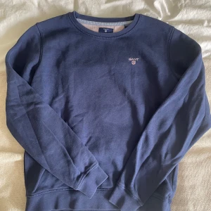 Mörkblå sweatshirt från GANT - Säljer en stilren mörkblå sweatshirt från GANT med broderad logga på bröstet. Tröjan har rund halsringning, långa ärmar och ribbade muddar. Perfekt för dig som gillar klassisk och enkel stil. Passar mig som är 170!