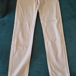 Beiga smala chinos från Boomerang - Snygga beiga chinos från Boomerang, modell Oscar, med smal passform och låg midja. Byxorna har smala ben och är tillverkade i bomull. Perfekta för dig som gillar en clean och stilren look. Byxorna är helt oanvända 