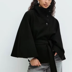 Gina tricot poncho/cape jacka! - Jätte snygg poncho/cape jacka från Gina tricot! Stora armar och knyt i midjan. Kan ha den öppen men också knäppt där uppe! I den svarta färgen. Storlek M/L. Helt ny med prislapp! Väldigt eftertraktad nu till hösten!!🍂💕