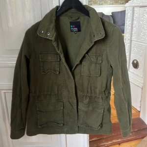 Olivgrön parkajacka från Even&Odd - Snygg olivgrön parkajacka från Even&Odd med fyra stora fickor framtill och markerad midja. Jackan har hög krage med tryckknappar och är perfekt för lager-på-lager-stil. Sitter som xs.