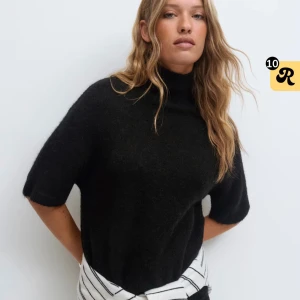Svart stickad polotröja med kort ärm - Svart stickad polotröja med korta ärmar och hög krage. Tröjan har en loose fit och är gjord i ett mjukt, fluffigt material som känns riktigt skönt mot huden. Perfekt för lager-på-lager och funkar året runt.🖤