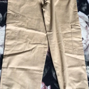 Beige cargopants från 157, stl M - Snygga beige cargopants från 157 i modellen Amelie. Byxorna har flera praktiska fickor på sidorna med knappstängning och är tillverkade i ett mjukt bomullstyg. Perfekta för en avslappnad och trendig look.