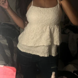 Vit strukturerad linnetopp med volang - Säljer en vit linnetopp med smala axelband och snyggt strukturerat tyg. Toppen har en volangliknande nederdel som ger en luftig och söt look. Perfekt till jeans eller kjol för en fräsch stil.