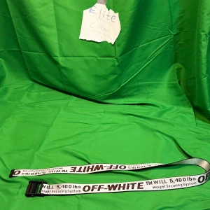 Off-White  vit/svart - Säljer ett ikoniskt Off-White industribälte i vit textil med svart spänne. Bältet har tydlig svart och röd text med märkets logga och detaljer som '5,400 lbs' och 'Weight Securing System'. Perfekt för att lyfta din streetwear-look.Liknande modell som originalet!
