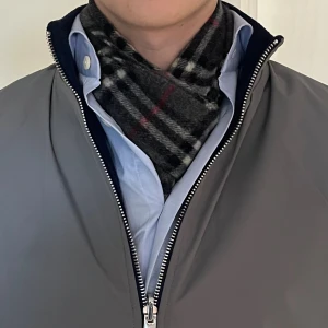 Rutig halsduk från Burberry i kashmir/ull - Snygg halsduk från Burberry i klassiskt rutigt mönster med grå, svart, vit och röda detaljer. Gjord i 50% kashmir och 50% ull, med fransar i ändarna. Perfekt accessoar för att lyfta din outfit under kyliga dagar.