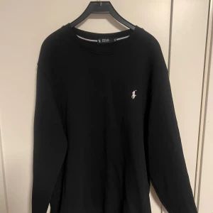Svart tröja från Polo Ralph Lauren XXL - Svart långärmad tröja från Polo Ralph Lauren i storlek XXL. Klassisk rund halsringning och diskret broderad logga på bröstet. Tröjan är i mjuk bomull och har en clean, stilren look som funkar till allt. Knappt använd, inga defekter eller sådant. Priset kan diskuteras. 