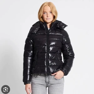 Svart glansig pufferjacka med huva - Svart pufferjacka med glansig finish och huva. Jackan har dragkedja framtill, två fickor med dragkedja och elastiska muddar vid ärmsluten. Perfekt för kalla dagar och riktigt snygg till jeans.Vid fler frågor eller fler bilder hör av er❤️pris går att diskutera 